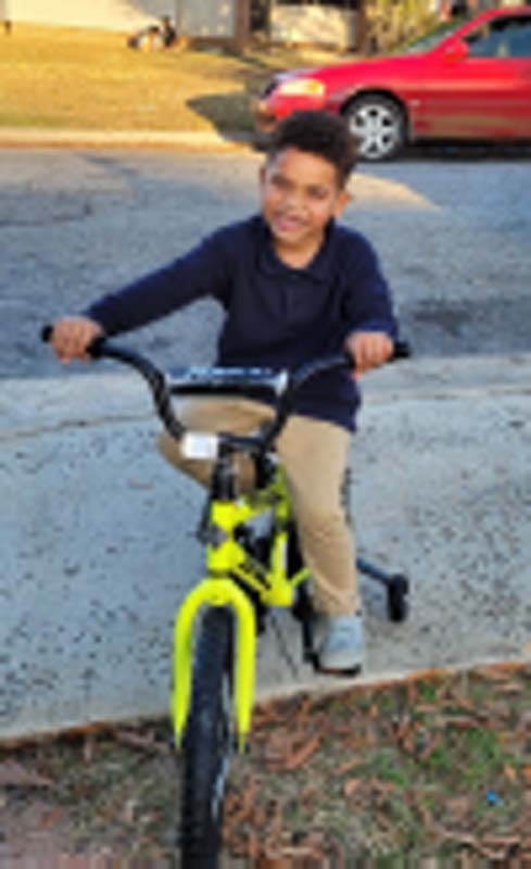 A little boy sits on his new bike and smiles with a missing front tooth. 